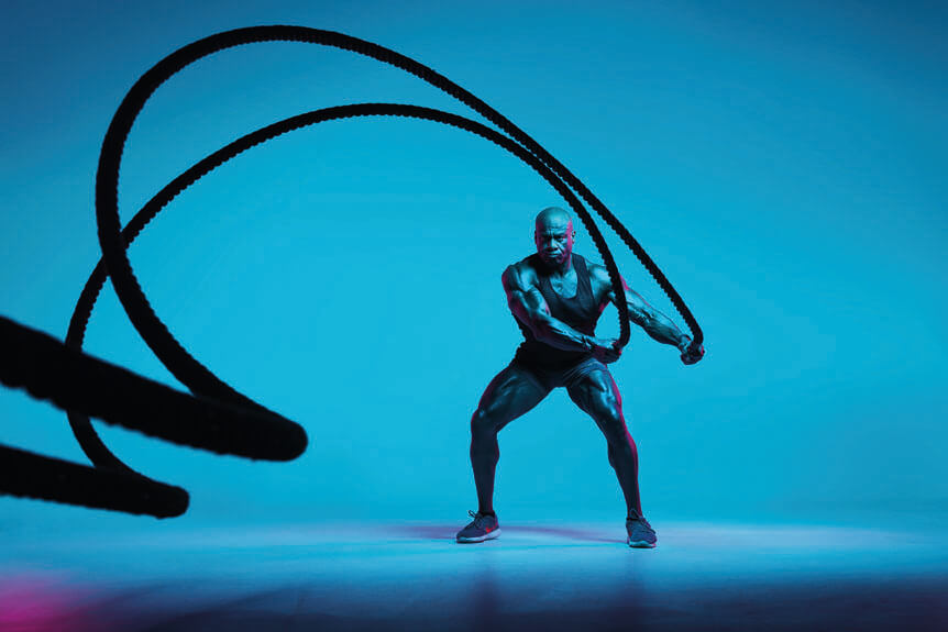 Muscular man swinging fitness ropes under blue lighting