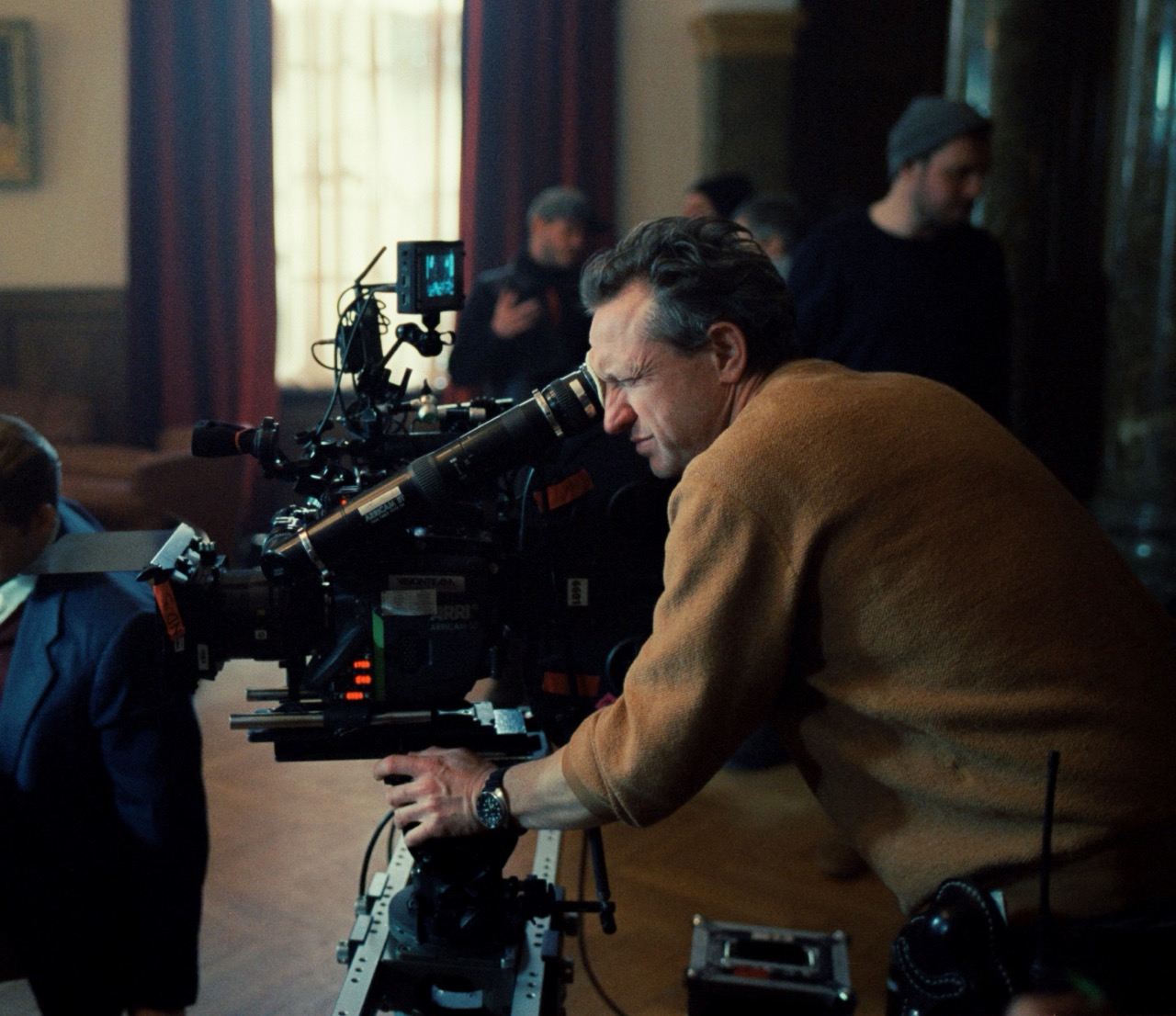 A man operates a camera, while crew members stand behind him