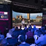 A conference with a person sitting in front of an audience on stage