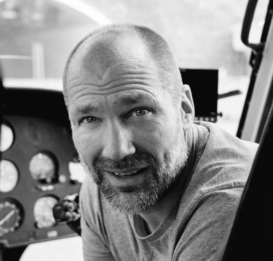 Black-and-white photo of a man smiling at the camera sitting in a car