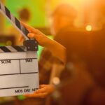 A person holding a clapper board in front of a green and orange blurred background