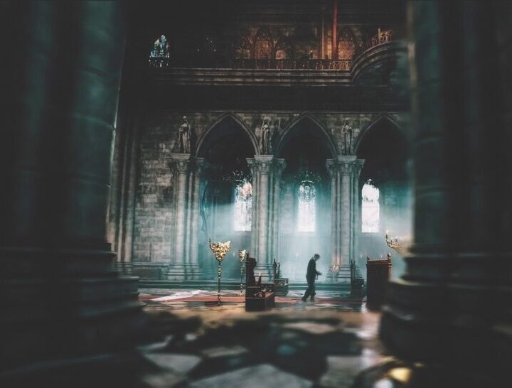 A person standing in a dimly-lit ornate room with large arches and old furniture