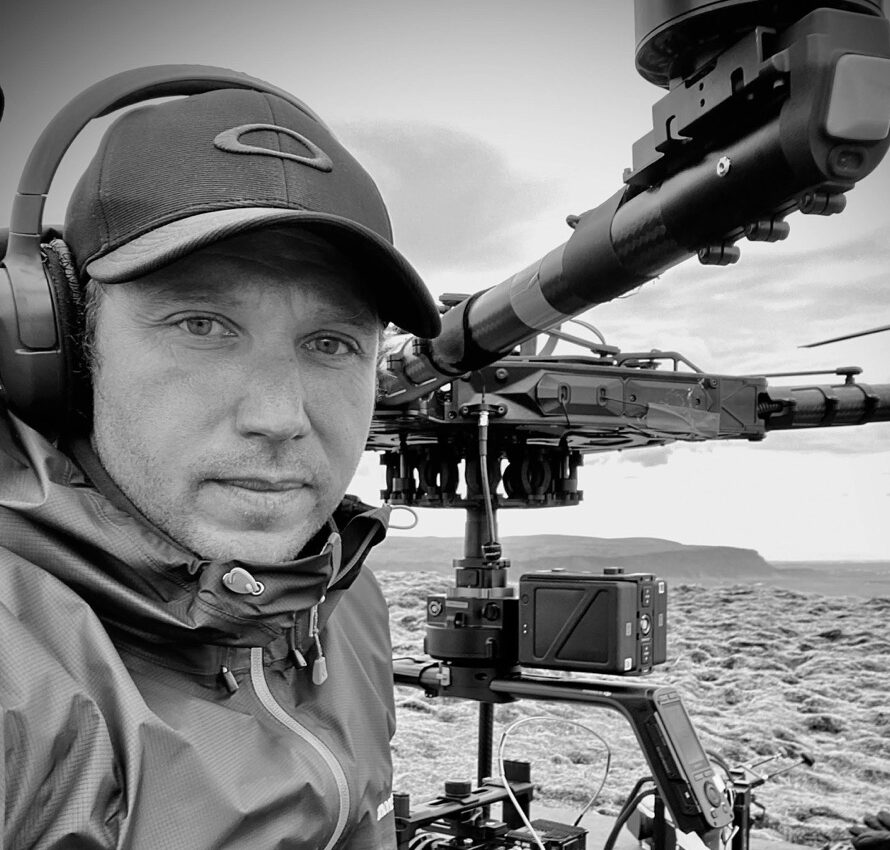 Black-and-white photo of a man wearing a hat and headphones standing next to equipment