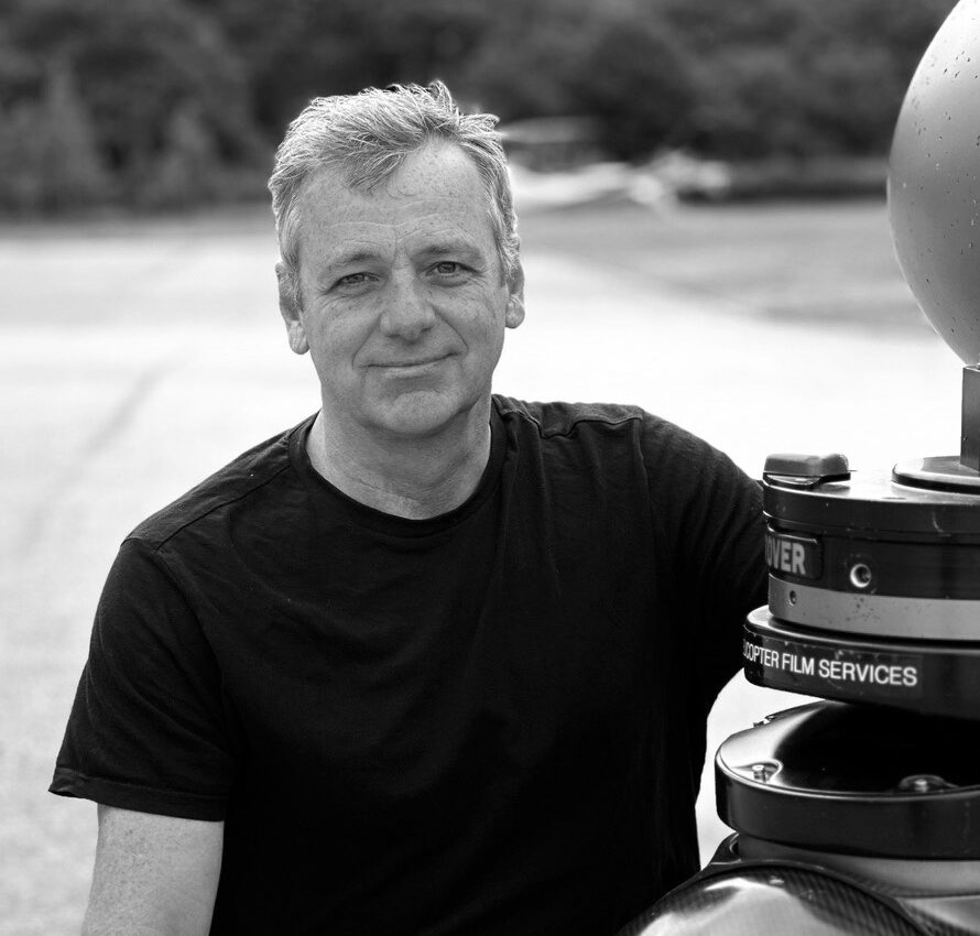 Black-and-white photo of a man wearing a t-shirt standing outside smiling at the camera