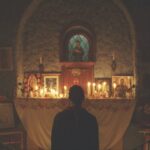 A person standing in front of a candle-lit altar in a dim room