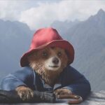 Paddington bear wearing a red hat and blue coat, climbing up a mountain