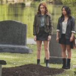 Two women standing in a cemetery looking at a newly dug grave