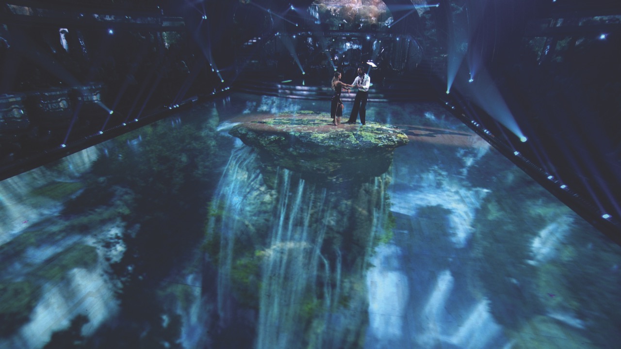 A couple standing on a projected floating island in the middle of a stage