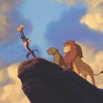 A screenshot of the cartoon “The Lion King”. A lion and lioness stand behind a mandrill holding a lion cub on a cliff