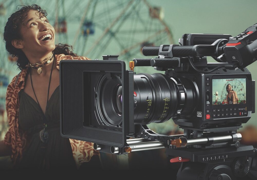 A woman looking upwards and smiling behind a professional filming camera. they are places in front of a blurred green background