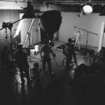 A black and white photo a film set where large lights and cameras are set up