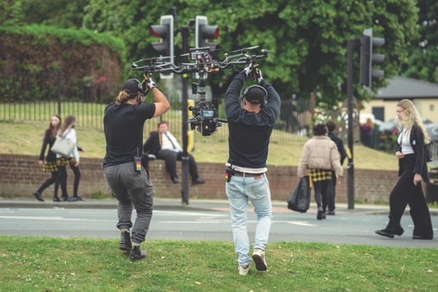 Two men lift up a drone camera in an open field