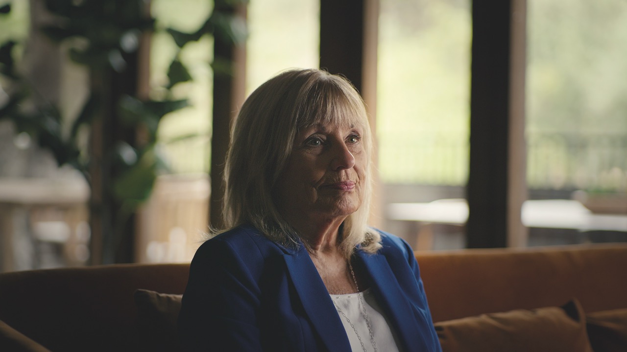 An older woman in a blue jacket with a somber expression