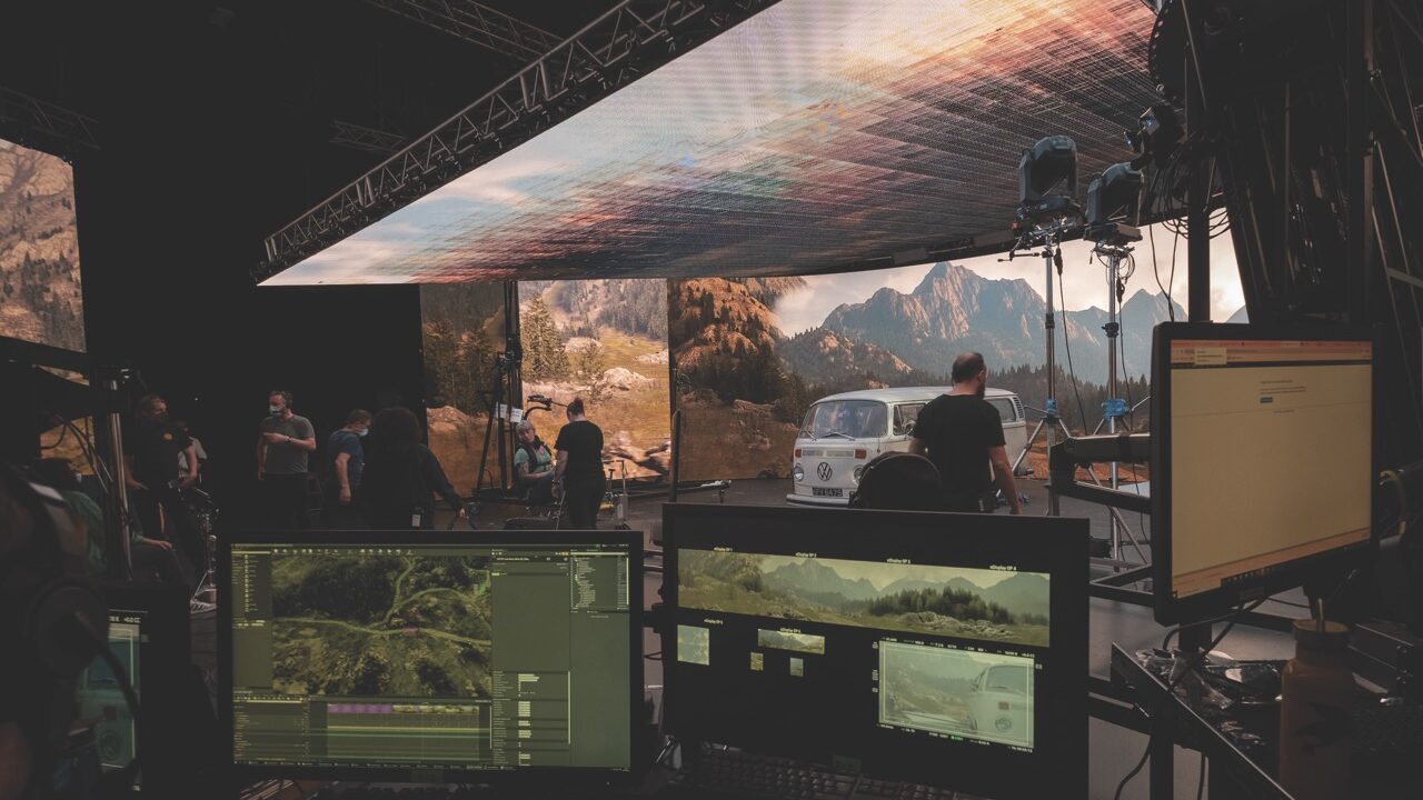 A film studio with large LED screens surrounding a camping van and on the ceiling. A group of people monitor the scene