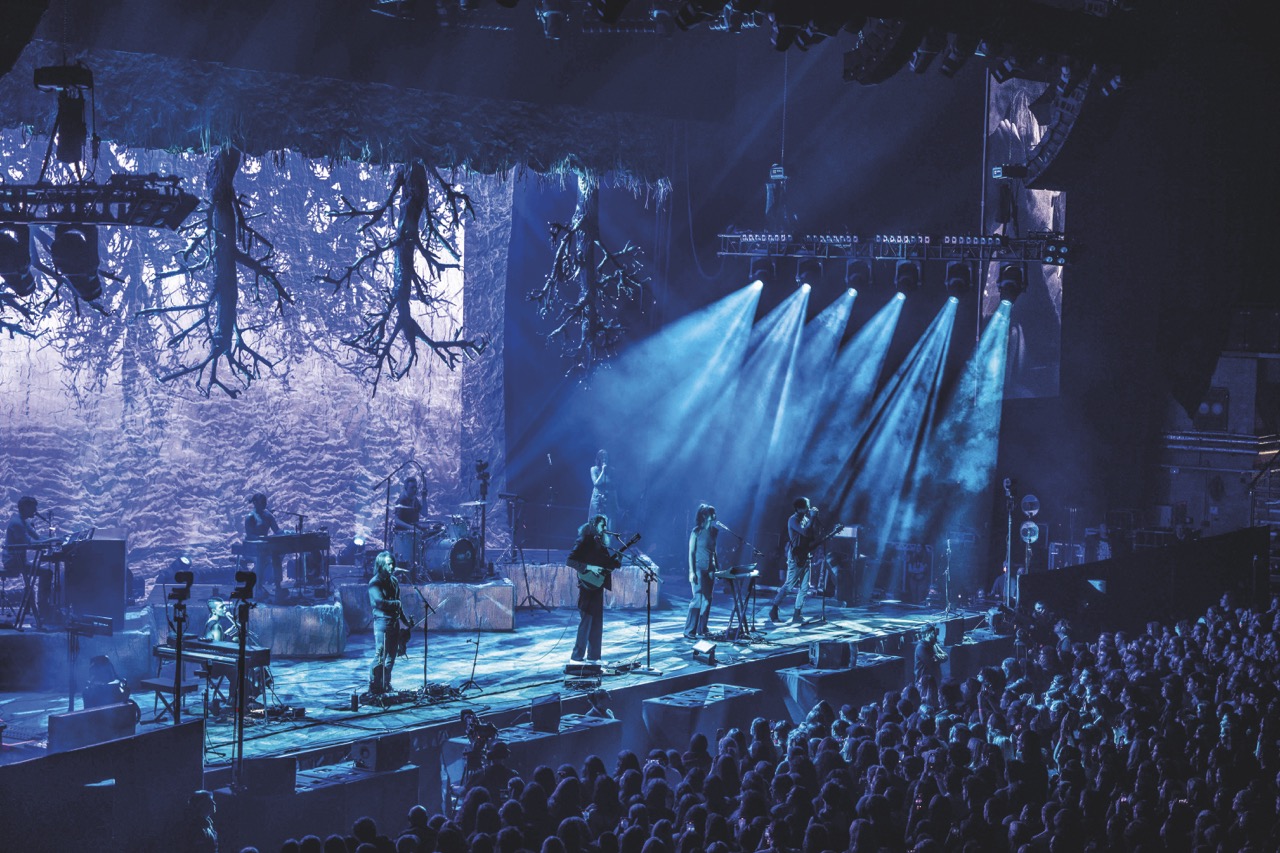 A band performing on a blue-lit stage in front of a busy audience