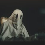 A person sitting on an ornate chair with a ghost sheet covering them