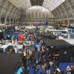 A busy conference hall with multiple stalls in a building with a curved roof