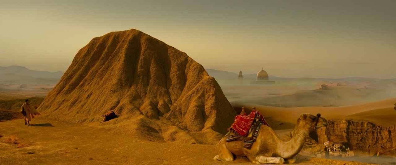 An orange mountain in a desert with a camel sitting in front
