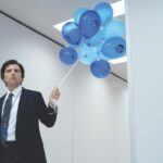 A man wearing a suit holding a bunch of blue balloons
