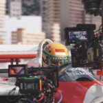 A person sitting in a race car with a camera on a mount filming them
