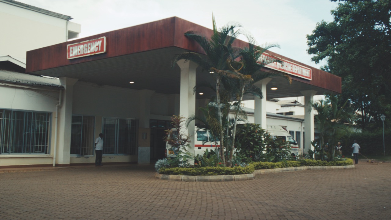 The outside of a hospital with trees and an ambulance outside. The building has a large red porch