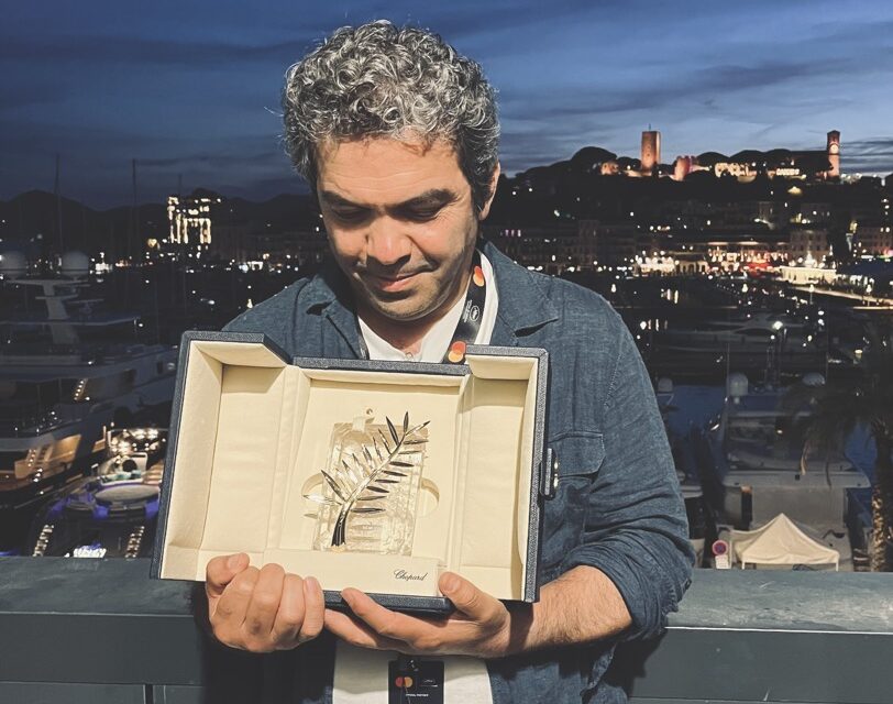 A man wearing a suit holds a certificate as he stands in front of a city skyline