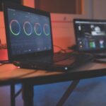 Two laptops sit on a desk with lots of cables attached in a dim red room