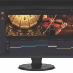 A large black monitor with a hooded rim. The screen shows a person playing the violin inside an ornate building
