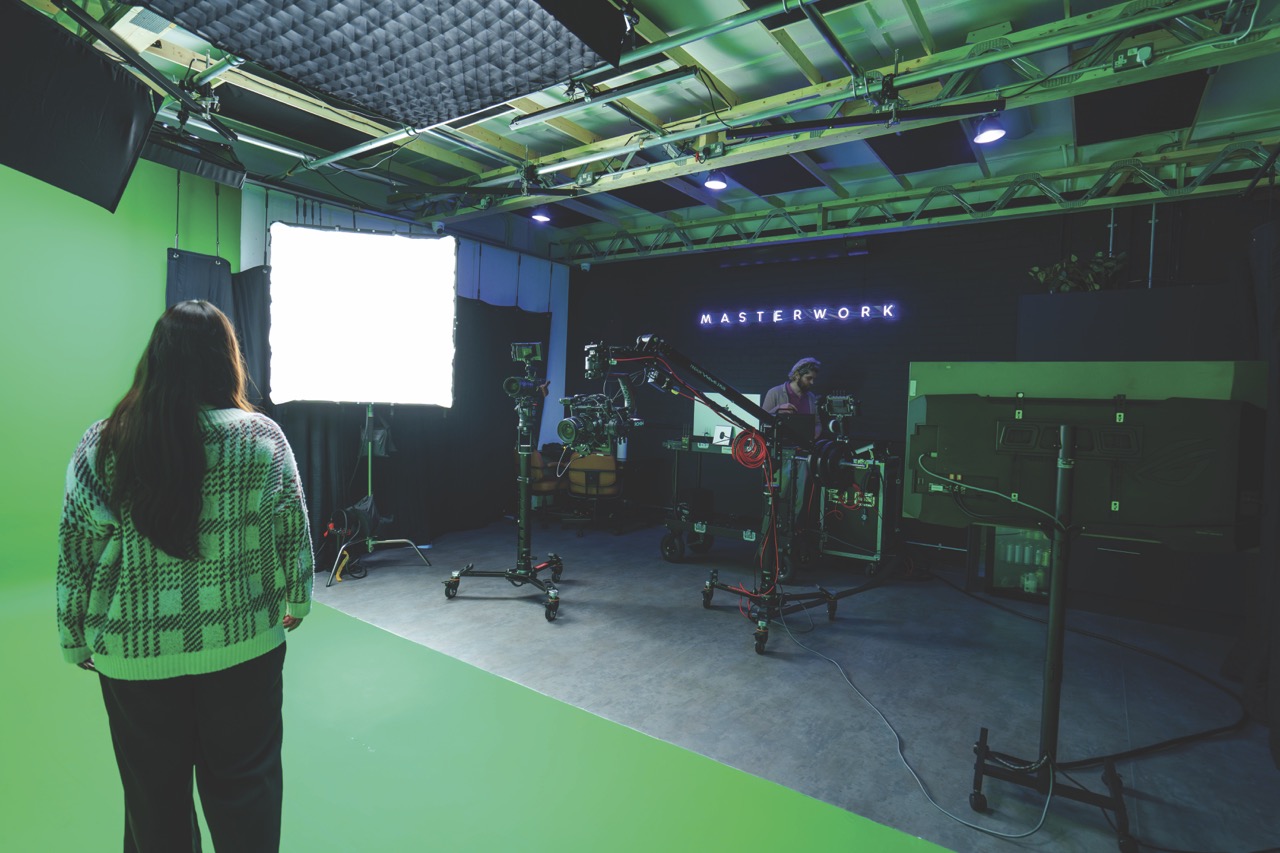 Over the shoulder of a woman standing on a green screen. She looks towards a large panel light