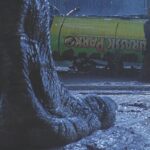 A large dinosaur foot in the foreground and two people crouch next to a toppled van in the background. The scene takes place at night and the ground is wet