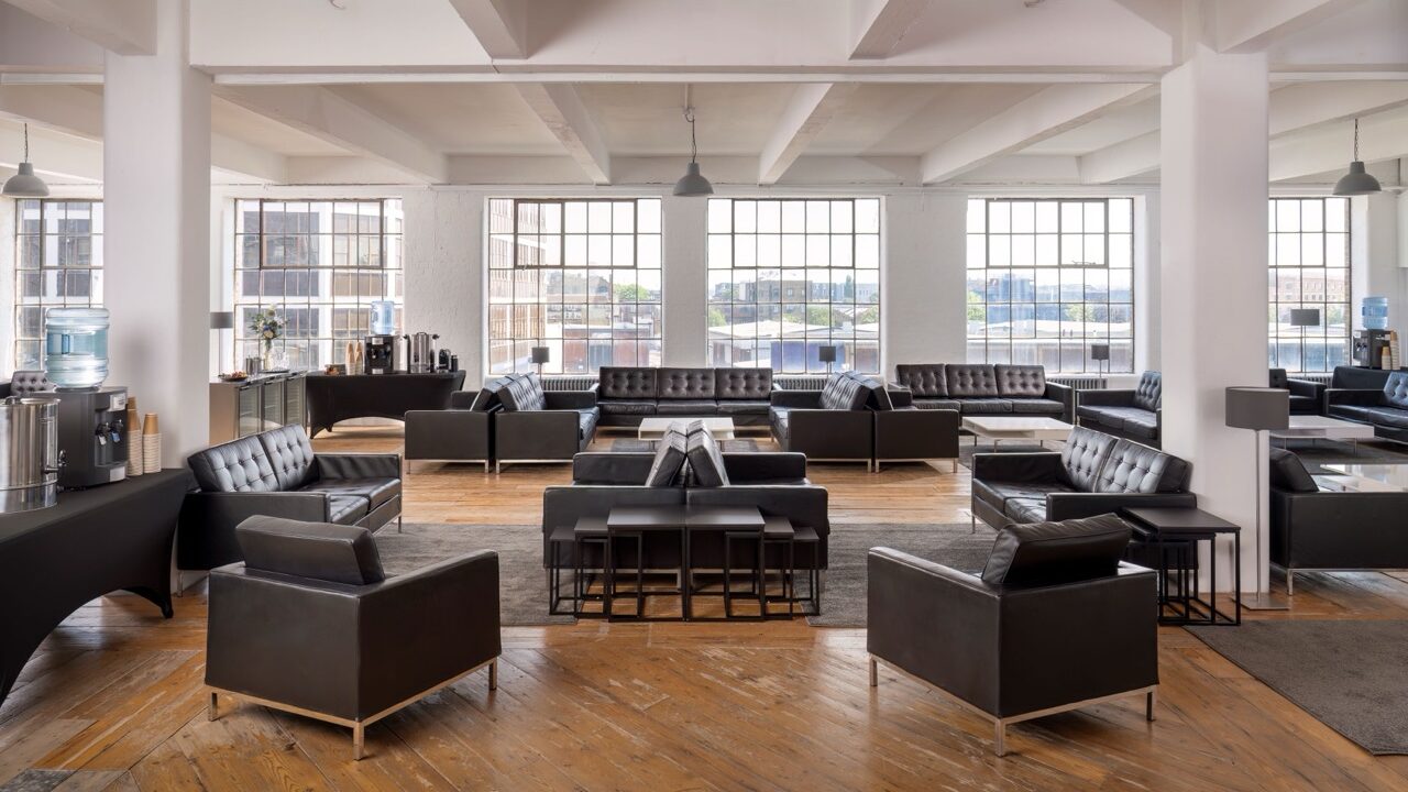 An empty room with large windows and groups of black leather sofas on wooden floor