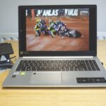 A laptop sitting at a wooden desk with motorbike racing on the screen. A portable SSD is attached with a wire
