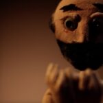 A handmade figurine of a man with a beard holding up his hands in orange lighting