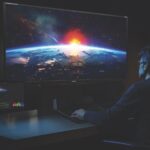 A man working at a large monitor in a dark room. The screen shots the earth from space