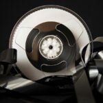A vintage film reel with streams of film lying around, against a black background