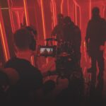 A production team filming actors in black suits and balaclavas standing in a red room