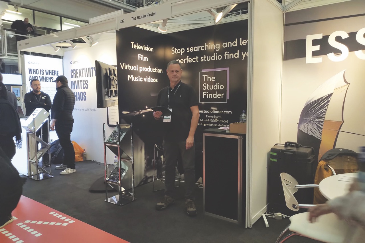 A conference hall with a man standing at a stall named The Studio Finder