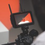 An Atomos monitor with two antennas filming a bottle on a table in an orange and white room