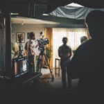 A living room with actors standing in the middle and a film crew around the outside