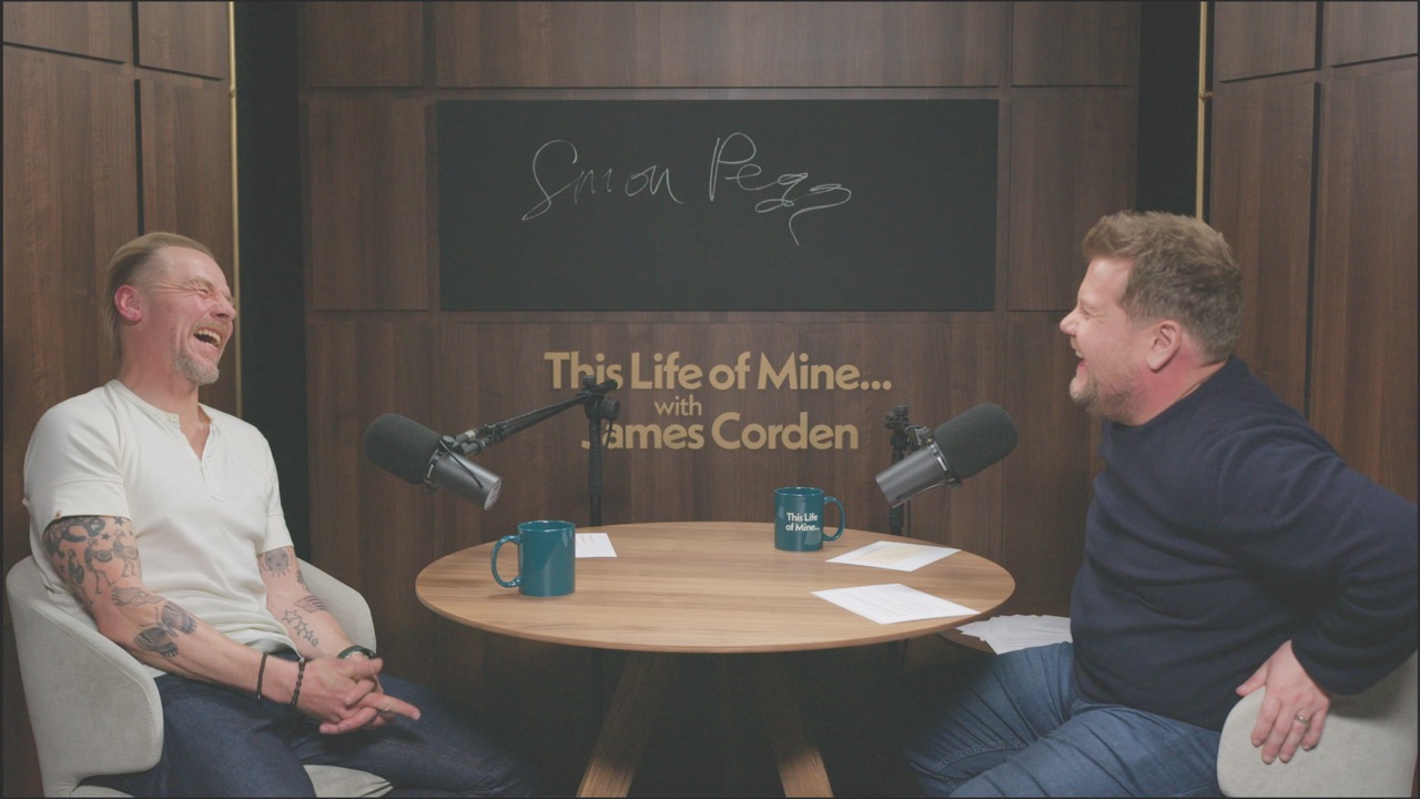 Two men sit at a round table doing an interview with microphones in front of them