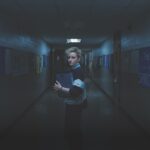 A woman stands in a dark school hallway with a scary mood