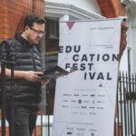 A man walking out of a building, carrying a brochure. He walks past a sign for CVP's Education Festival