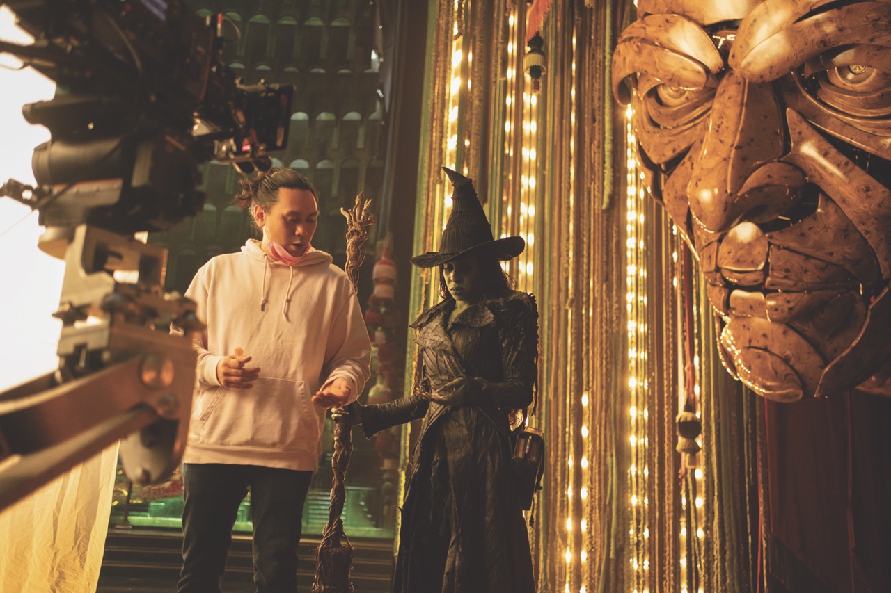 A photo of a director working with a woman dressed as a witch on the set of Wicked