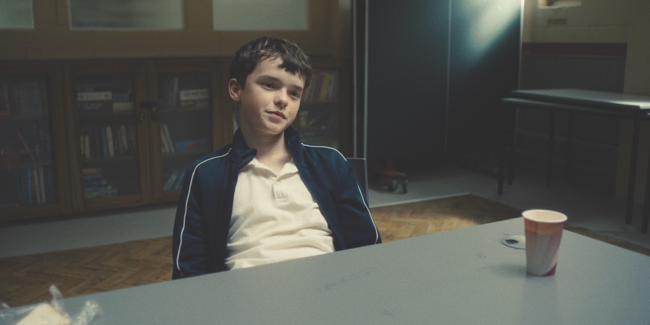 A still from Adolescence showing a young boy slouching at a table