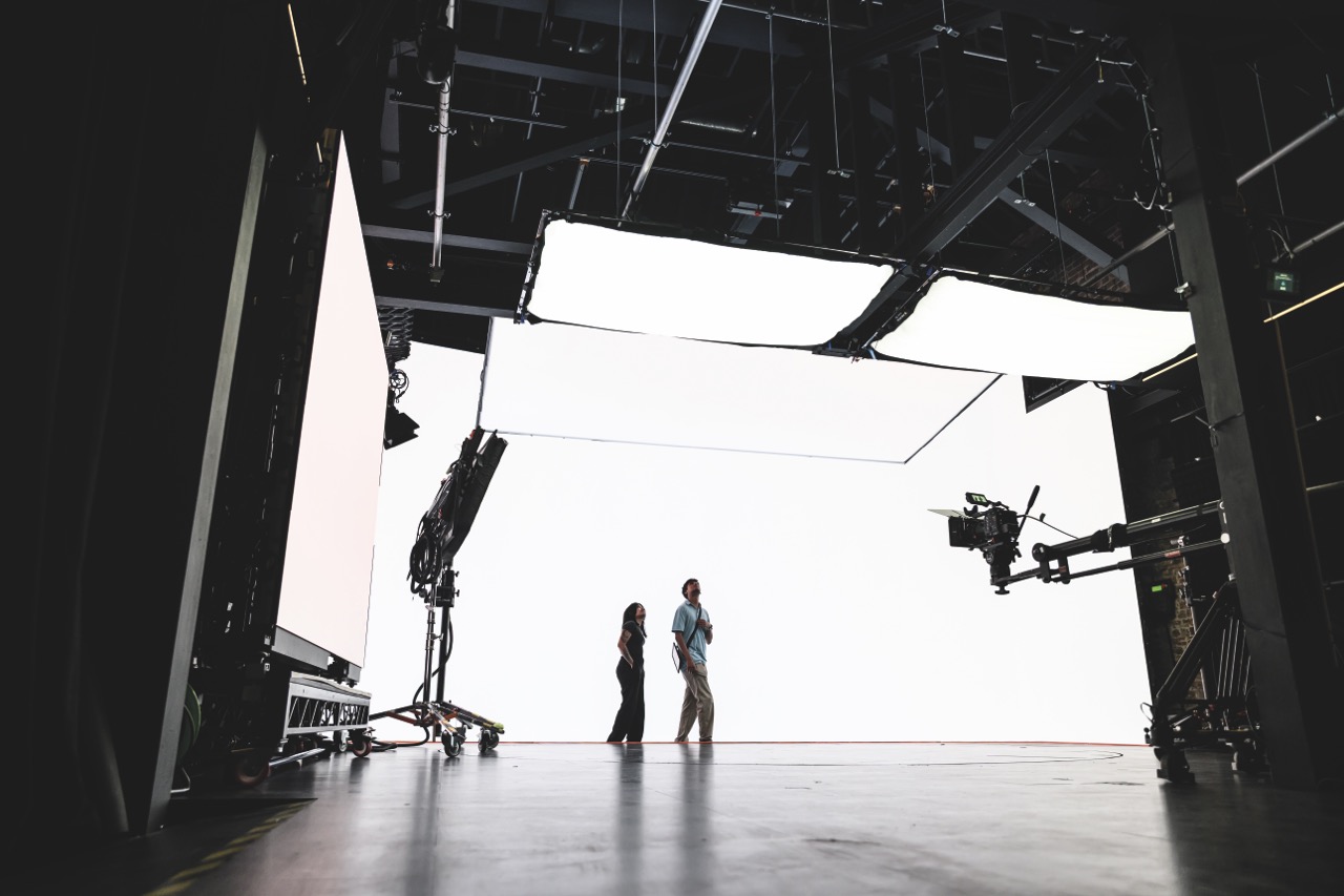 A black and white photo of Film Soho's studio space. Figures stand in the middle of the space