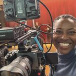 A young woman smiling and operating a professional camera in a theatre