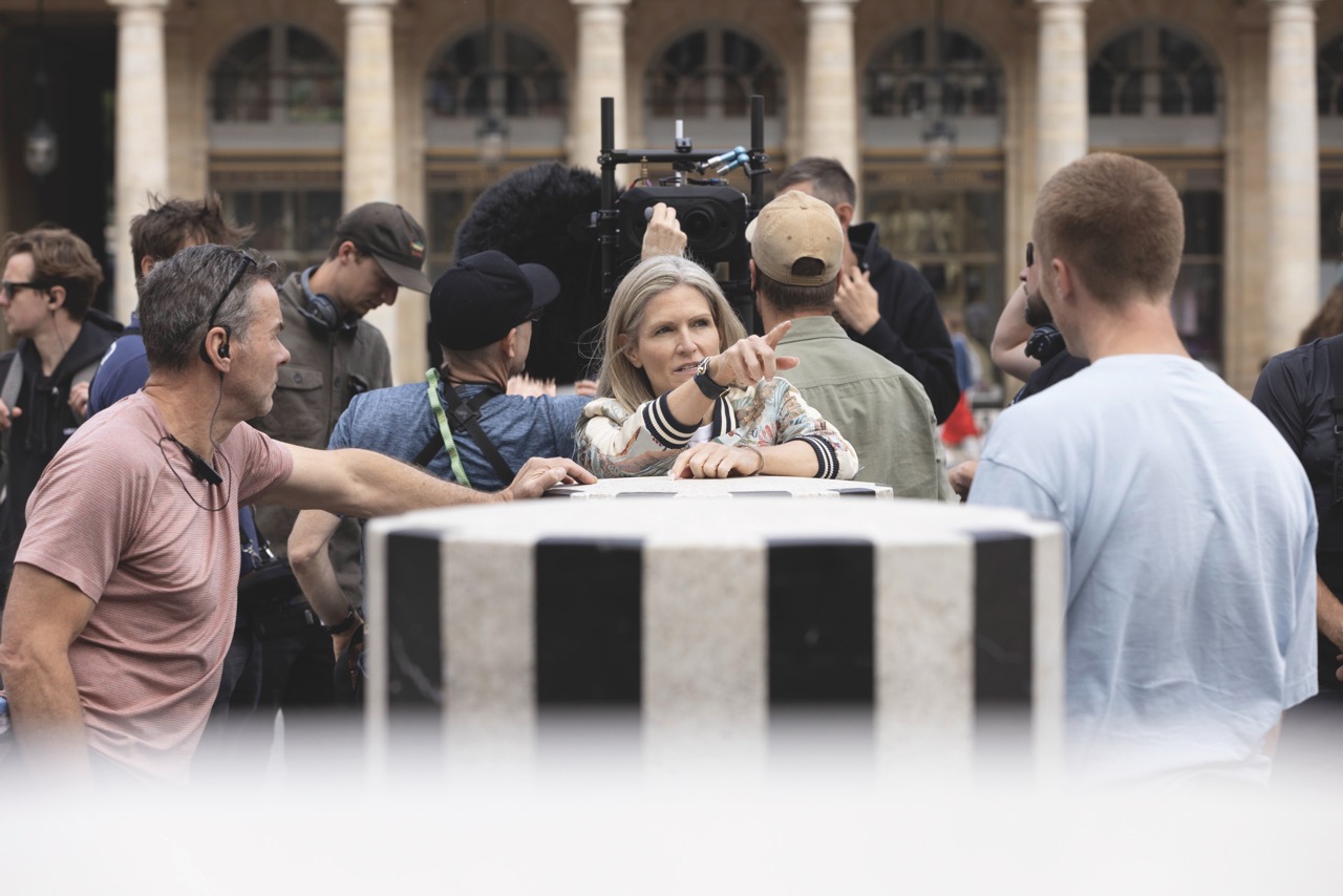 A woman standing next to a bollard and pointing, surrounded by a filming crew