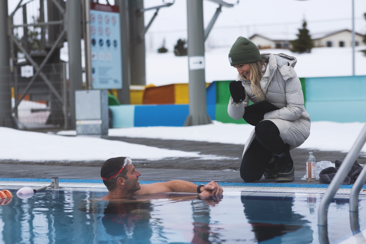 A woman in a winter gear talking to a man in a swimming pool