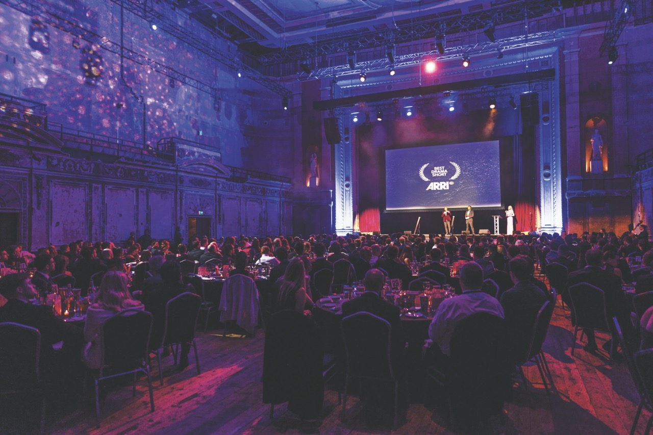 A large crowd at the International Motor Film Awards with a stage and screen at the front