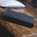 A black Samsung storage device resting at an angle on a wooden desk next to a computer mouse